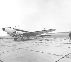 Full view of R4D aircraft at airport, four people standing to right