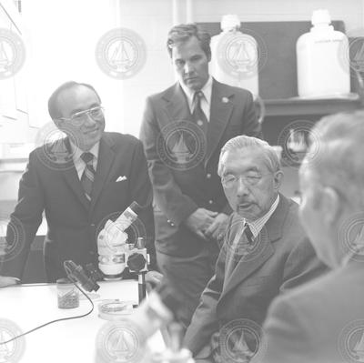 Visiting Emperor Hirohito seated at microscope.