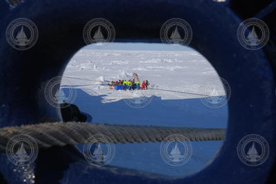 A hawsehole in the bow frames the workers on the ice.