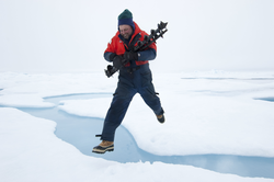 John Kemp, carrying drill bits, jumps across an ice stream.