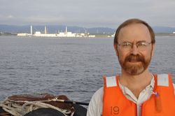 Ken Buesseler standing on a research vessel Japan coastline in background.