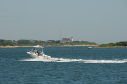 A small power boat passing through Great Harbor in front of Nobska Point.