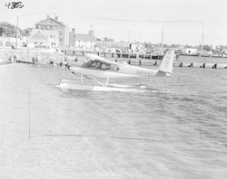 Helio courier on shore, dock and buildings in background