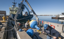 Ian Hanley and Jim Dunn load a hydrophone buoy onto Tioga for deployment.