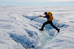 Laura Stevens jumping over a stream over meltwater atop the Greenland Ice Sheet.