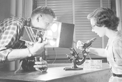 Roberta Claire (Eike) Blanchard in lab with Henry Johnson, filming microscope