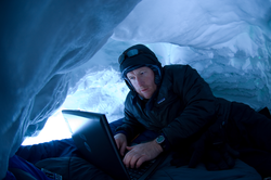Hugh Powell typing on laptop in a snow cave.