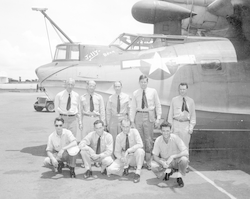 Group of nine men in front of PBY aircraft.