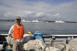 Ken Buesseler standing on a research vessel Japan coastline in background.