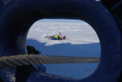 A hawsehole in the bow frames the workers on the ice.
