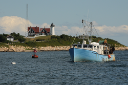 A fishing boat with Nobska Point and lighthouse in the background.