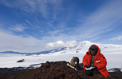 Andrea Burke sitting on lava rock taking field notes in Antarctica.