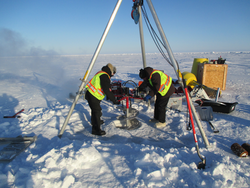 Kris Newhall and John Kemp using an auger to drill an ice hole for an ITP installation.