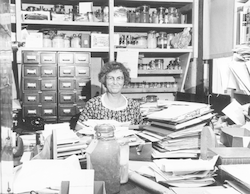 Mary Sears posing behind stacks of work.