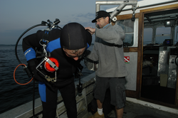 Pat Lohmann assisted by Rocky Geyer prior to his dive to search for a tripod.