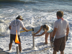 Becky Gast holds the core cylinder as Bill Boyd drives it into the sand.