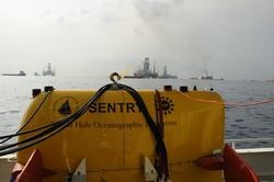 AUV Sentry on deck of Endeavor with oil spill activities in background.