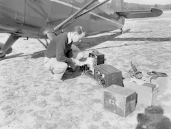 Working with equipment on ground next to Stinson aircraft