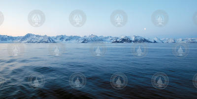 Mountains and a moon rise over mountains on the east coast of Greenland.