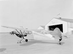 Full view of Stinson aircraft at airport, hangar in background