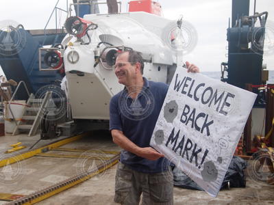 Mark Kurz holds a "welcome back" sign after his first Alvin dive shower.