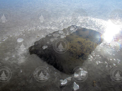 Water and mud below a hole in a frozen freshwater pond.