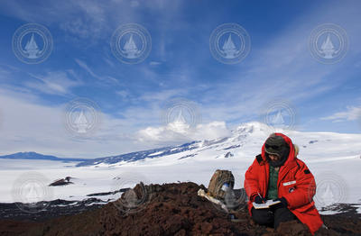 Andrea Burke sitting on lava rock taking field notes in Antarctica.