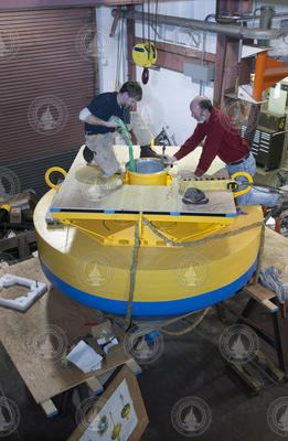 Mike McCarthy and Neil McPhee working on top of buoy in shop.