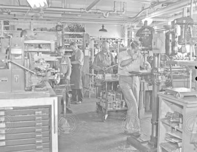 Machine shop in Bigelow Laboratory full of men working.
