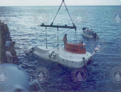 Sea Cliff and small boat in water, group watching from dock