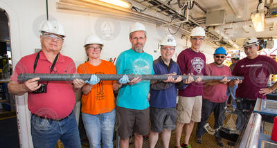 Researchers holding a long single continuous piece of hard rock core.
