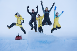 A group of researchers jumping off an ice mound in Antarctica.