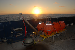 Ocean bottom seismometer on deck in front of sunset.
